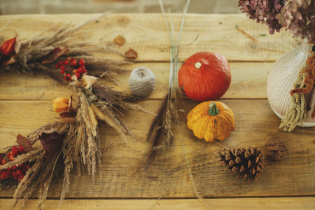 Stylish autumn wreath on rustic table. Fall decor and arrangement in farmhouse. Rustic autumn wreath with dried grass, berries, herbs on wooden table with pumpkins and pine cone.の写真素材