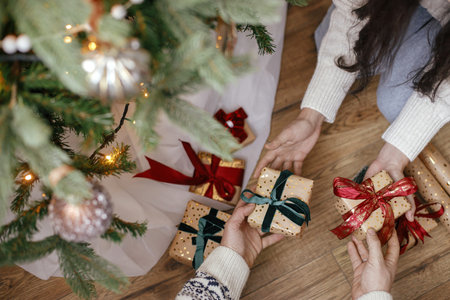Hands exchanging christmas gifts under christmas tree in festive decorated room. Merry Christmas and...