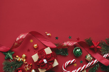 Modern christmas flat lay. Stylish christmas gift, baubles, fir branches, confetti and candy cane on red background. Merry Christmas! Seasons greeting card template, space for text.  Winter holidaysの写真素材