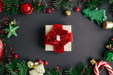 Merry Christmas and Happy Holidays! Stylish christmas gift flat lay and branches, red berries, gold ornaments frame on black background. Season's greeting card, winter holidaysの写真素材