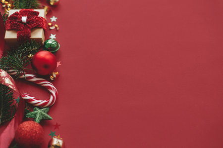 Merry Christmas! Modern christmas still life. Stylish christmas gift, baubles, fir branches, confetti on red background. Seasons greeting card, space for text. Winter holidays bannerの写真素材
