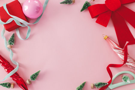 Pink Christmas. Modern Christmas flat lay with red bow, baubles, little green trees and ribbons on pink background. Creative christmas background with space for text, seasons greetings.の写真素材