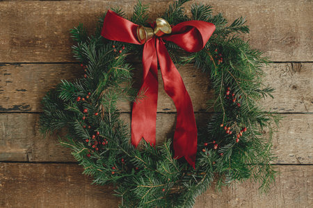Christmas wreath flat lay.Stylish christmas wreath with red ribbon, red berries and golden bells on rustic wooden table. Winter holiday decor. Merry Christmas and Happy Holidays!の写真素材