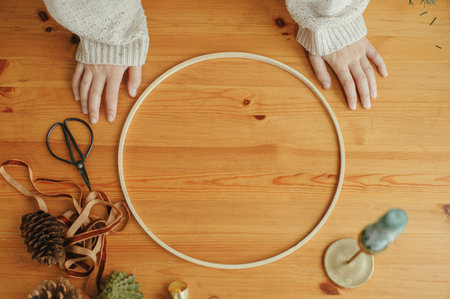Making modern christmas wreath. Woman hands on table with round hoop, ribbon, candle, pine cones, scissors. Festive workshop. Winter holiday decorの写真素材