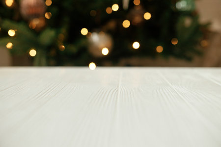 Wooden table close up on background of christmas tree with golden lights bokeh. Christmas festive template and mock up for product. White wooden board against illuminated festive room with treeの写真素材