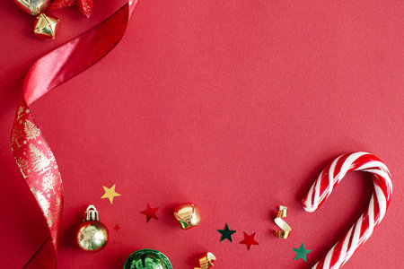 Modern christmas flat lay. Stylish christmas candy cane, confetti and ribbon border on red...
