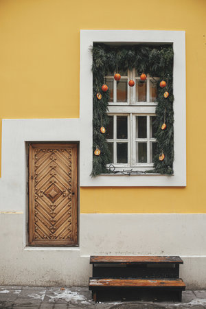 Stylish christmas branches with oranges and tangerines on white window of yellow building. Modern simple eco christmas decor in city street. Winter holidays in Europe. Merry Christmasの写真素材
