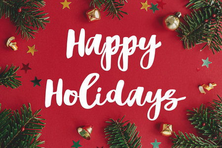 Happy Holidays text sign on christmas baubles, fir branches and confetti frame on red background...