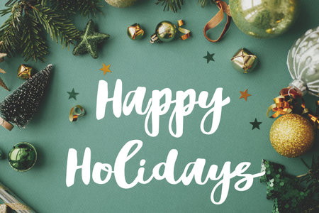 Happy Holidays text sign on christmas flat lay with golden festive decorations, confetti, gift, fir branches on green background. Season's greeting card. Christmas postcardの写真素材