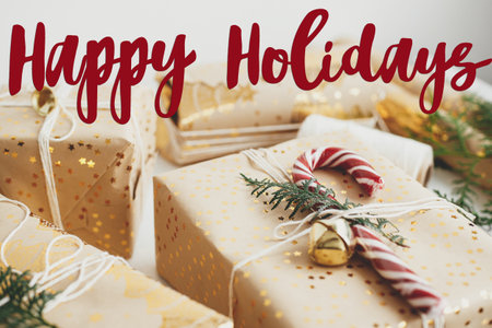 Happy Holidays text sign on christmas gift box with candy cane, fir branch, festive paper and golden ornaments on white wood. Season's greeting card. Christmas postcardの写真素材