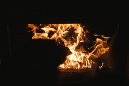 Close up of burning wood in fireplace in dark evening room. Fireplace heating in house, electricity blackout. Atmospheric time at fireside in homeの写真素材