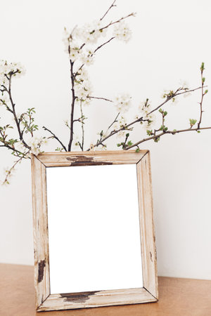 Photo frame mockup and blooming cherry branches on wooden table against white wall. Empty picture frame template and spring flowers. Simple countryside living. Space for textの写真素材