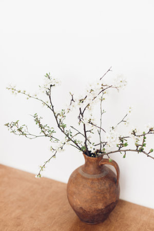 Blooming cherry branches on wooden table against white wall. Spring flowers in vintage vase still life. Simple countryside living, home rustic decor. Space for textの写真素材