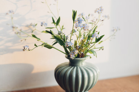 Beautiful little blue flowers in vase in warm sunlight on rustic wooden background. Delicate myosotis petals, forget me not spring flowers. Atmospheric evening moment. Simple countryside livingの写真素材