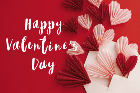 Happy valentines day text on envelope with red and pink hearts flat lay on red paper background. Modern Valentines day greeting card. Handwritten signの写真素材