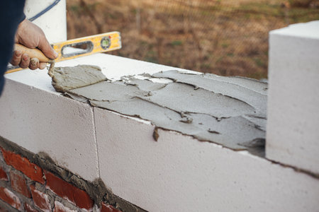 Worker laying autoclaved aerated concrete blocks, working with adhesive and trowel. Builder...