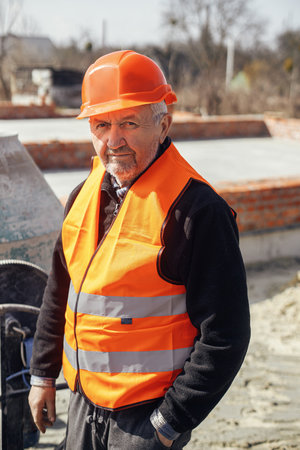 Senior foreman in hard hat standing on background of bricks masonry with cement on concrete...