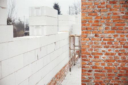 Masonry autoclaved aerated concrete blocks and bricks on concrete foundation. Laying walls with white blocks. Process of house building at construction siteの写真素材
