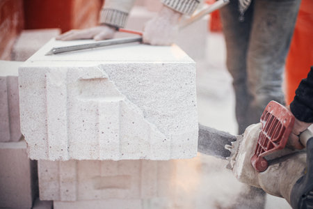 Workers cutting autoclaved aerated concrete block with chainsaw closeup. Builders cutting white blocks for masonry installation. Process of house building at construction site.の写真素材