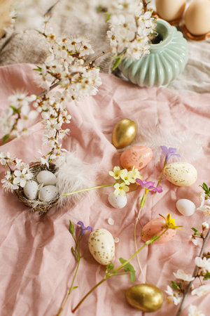 Happy Easter! Stylish easter eggs and blooming spring flowers on pink linen fabric. Modern eggs in nest, feathers and cherry blossoms. Rustic easter still lifeの写真素材