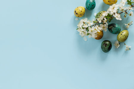 Stylish easter eggs and blooming flowers on blue background flat lay. Happy Easter! Natural painted...