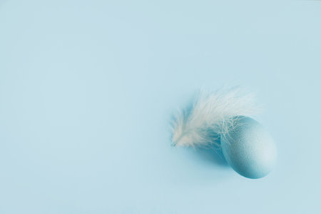 Stylish easter egg and feather on blue background flat lay. Minimal Easter still life. Modern greeting card or banner, copy space. Happy Easter! Natural painted blue eggの写真素材