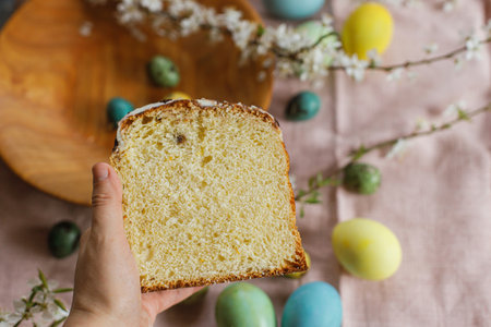 Hand holding half of baked easter cake on background of natural dyed easter eggs with spring flowers...