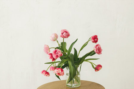 Stylish beautiful pink tulips bouquet in vase on wooden table in rustic room. Floral arrangement in farmhouse. Spring flowers composition, copy space. Happy mothers day and womensの写真素材