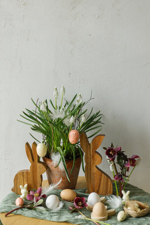 Happy Easter! Stylish wooden bunny, spring flowers, natural eggs and feathers on rustic table in...