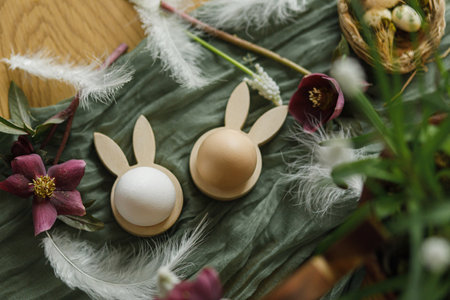 Happy Easter! Stylish wooden bunny ears and natural eggs, spring flowers, feathers and nest on rustic table close up. Easter still life. Festive arrangement and decor in farmhouse, top viewの写真素材