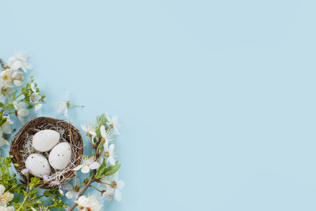 Stylish Easter eggs in nest and cherry blossoms flat lay on blue background with copy space. Happy...