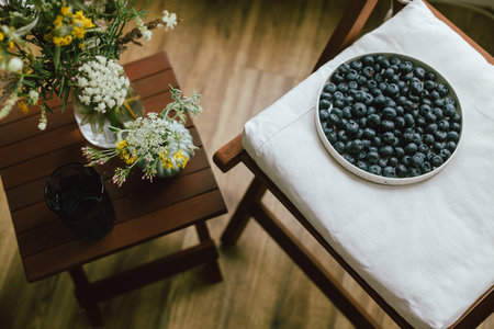 Fresh blueberries on modern ceramic plate and wildflowers bouquet in rustic room. Summertime in countryside. Healthy food aesthetics. Summer berriesの写真素材