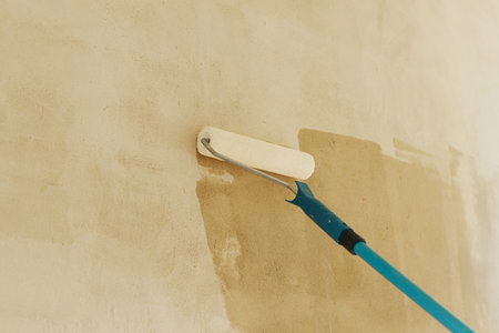 Worker priming walls in new building. Roller brush with prime covering plaster walls. Construction of house and home renovation concept.の写真素材