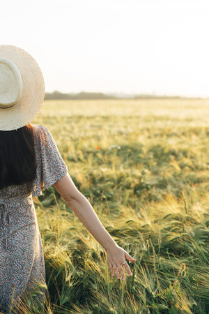 Beautiful woman in floral dress walking in barley field in sunset light. Atmospheric moment, rustic...