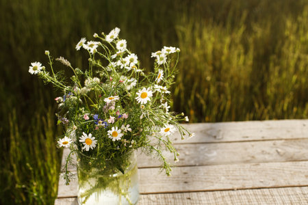 Beautiful wildflowers bouquet in sunlight on rustic wooden table in garden among grass. Beautiful summer flowers in vase gathered from garden, arrangement in countryside home. Copy spaceの写真素材