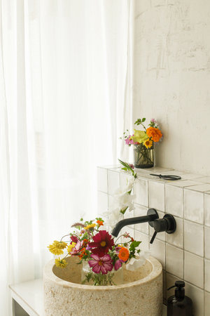 Beautiful flowers in modern bathroom with stylish sink, black faucet and white tiles. Summer flowers arrangement gathered from garden in modern room in homeの写真素材