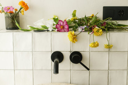 Beautiful flowers in modern bathroom with stylish sink, black faucet and white tiles. Summer flowers arrangement gathered from garden in modern room in homeの写真素材