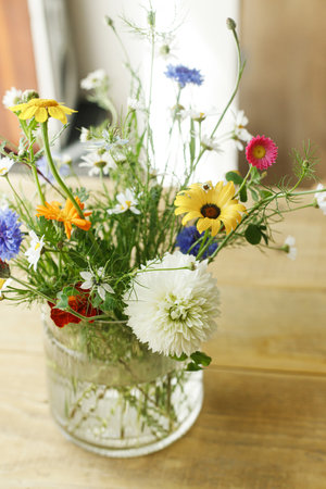 Stylish wildflowers bouquet in sunlight on rustic wooden table. Beautiful summer flowers in vase gathered from garden, floral arrangement in countryside homeの写真素材