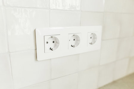 Stylish white electric socket close up installed on square tiles wall in kitchen in new scandinavian...