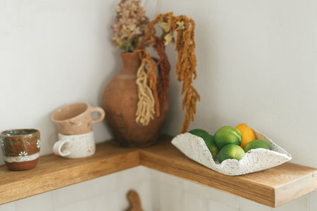 Limes in bowl on wooden shelf on background of utensils and cups on rustic wall in modern white kitchen in new scandinavian house. Modern kitchen interior and accessoriesの写真素材