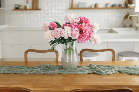 Beautiful peonies in vase on wooden table on background of stylish white kitchen with appliances in new rustic farmhouse. Modern kitchen interior. Minimal kitchen designの写真素材