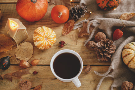 Autumn flat lay. Warm cup of tea, pumpkins, fall leaves, candle, cozy scarf on rustic wooden table....