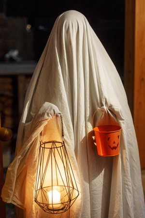 Trick or treat! Spooky ghost holding glowing lantern and halloween candy bucket in doors in dark....