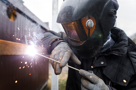 Shielded metal arc welding. Worker welding metal with electrodes, wearing protective helmet and gloves. Close up of electrode welding and electric sparksの写真素材