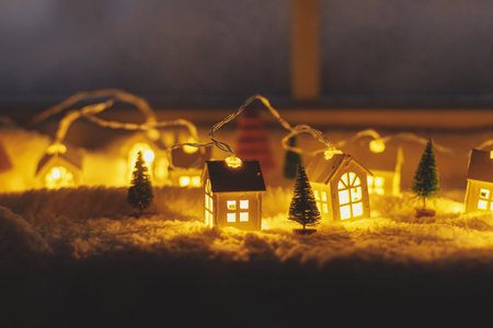 Cozy christmas miniature village. Stylish cute little glowing houses and christmas trees on soft snow blanket with lights in evening room. Atmospheric winter village still life. Merry Christmas!の写真素材
