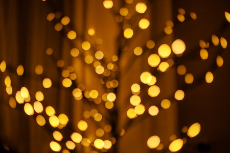 Blurred christmas golden lights bokeh. Bokeh of modern minimal glowing tree branches in evening cozy room, copy space. Happy Holidays! Festive illumination. Christmas bannerの写真素材