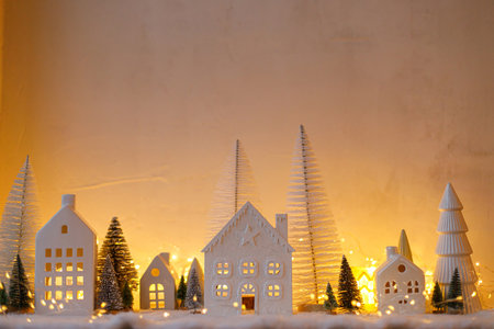 Atmospheric miniature christmas village. Stylish little white houses and trees on snow blanket with glowing lights in evening. Christmas modern winter village, holiday banner. Happy Holidays!の写真素材