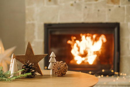 Stylish christmas wooden trees, star, pine cones and fir branches on table against burning fireplace. Modern rustic eco friendly decor for winter holidays in farmhouse living roomの写真素材