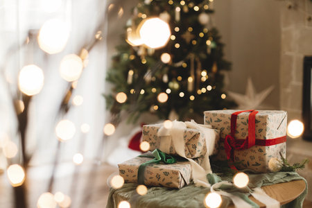 Stylish wrapped christmas gifts with ribbon on table on background of decorated christmas tree, rustic fireplace and festive lights. Merry Christmas! Atmospheric winter holidaysの写真素材