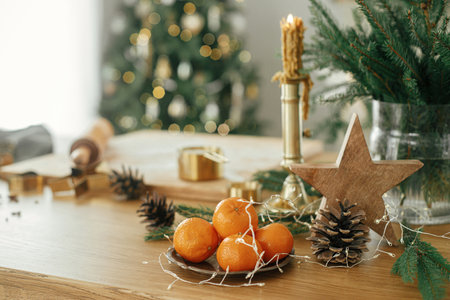 Making christmas gingerbread cookies. Wooden star, oranges, golden metal cutters, cooking spices and festive decorations on rustic table against stylish decorated christmas treeの写真素材